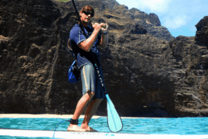 man on stand up paddleboard doing the shaka with Kauai mountains in the background