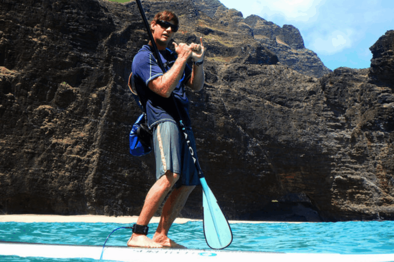 man on stand up paddleboard doing the shaka with Kauai mountains in the background